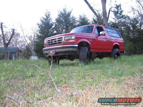 Red 1992 Ford Bronco parked on a grassy hill with trees in the background