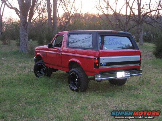 Red Ford Bronco parked on grass, rear view. Aftermarket wheels and tires are visible