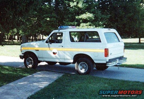 White 1992 Ford Bronco with yellow stripe and emergency lights parked on asphalt