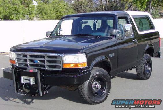 Black Ford Bronco with a white removable top, aftermarket front bumper with a winch, and black wheels