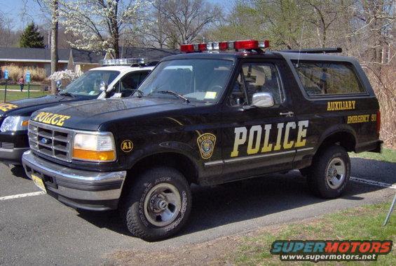 1992 Ford Bronco police SUV with "POLICE" and "AUXILIARY EMERGENCY 50" text, parked next to another police vehicle