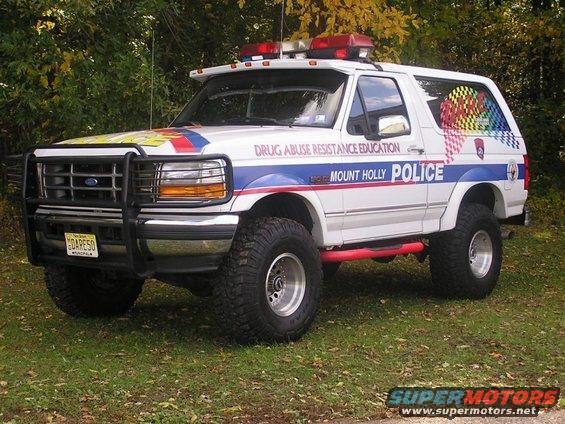 White 1992 Ford Bronco police SUV with "Mount Holly Police" text and rainbow checkered pattern on rear window