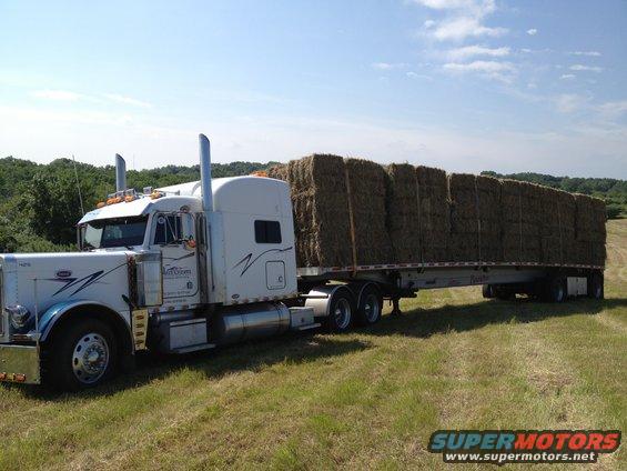 2003 Peterbilt 379 semi-truck with a flatbed trailer loaded with hay bales, parked in a grassy field