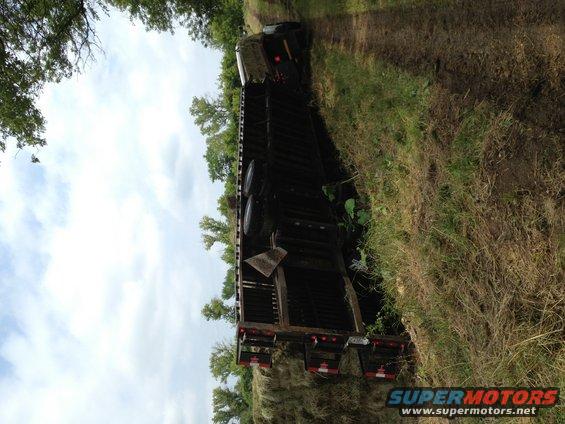 Tractor-trailer tipped on its side in a grassy ditch, with trees in the background