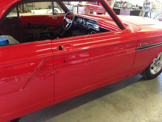 Side view of a red 1964 Ford Fairlane with interior visible. The door panel is off, showing the car's innards