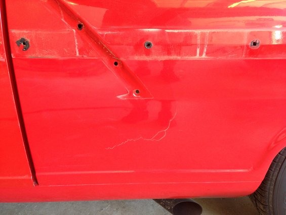 Red car door and fender with visible cracks in paint and mounting holes