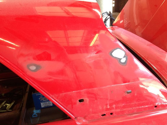 Red car hood with body filler patches and mounting holes