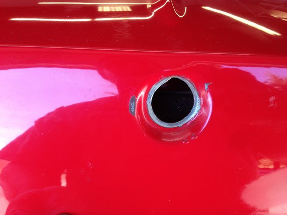 Close-up of a red car's fuel filler hole, showing raw metal around the opening