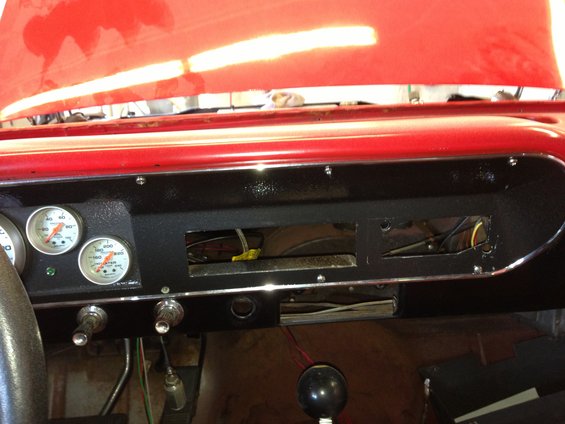 Car dashboard showing two gauges, switches, and an open radio slot. Red hood is visible above