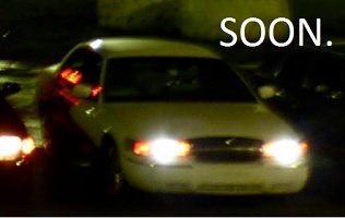 Front view of a white sedan at night with headlights on. Text reads 'SOON.'
