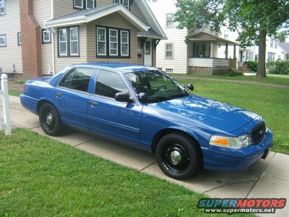Blue 2009 Ford Crown Victoria sedan parked on a driveway, front passenger side visible, with black steel wheels and a police-style light bar mount on the roof