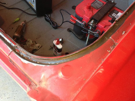 Red car door edge with rust and peeling paint, next to a car battery and charger