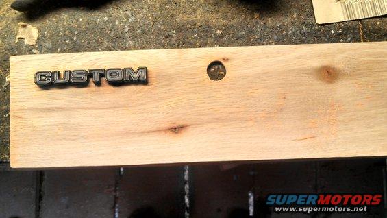 Custom badge on a light-colored wooden plank with a hole drilled next to it