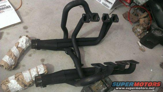 Black exhaust headers with four pipes each, some ends wrapped in paper