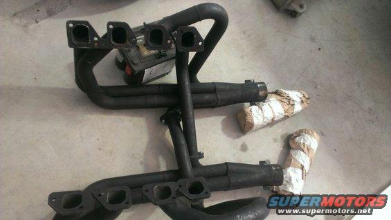 Two sets of black exhaust headers and mufflers on a concrete floor