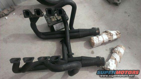 two sets of black exhaust headers and mufflers on a concrete floor, some wrapped in paper