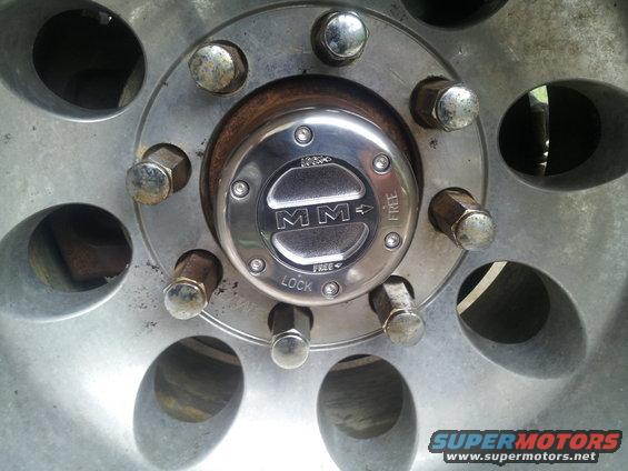 Wheel hub with MM logo, showing lock and free positions, surrounded by lug nuts and wheel spokes