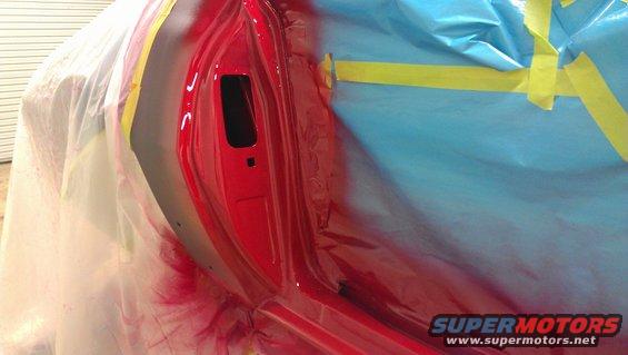 Red car door being painted, masked with blue plastic and yellow tape