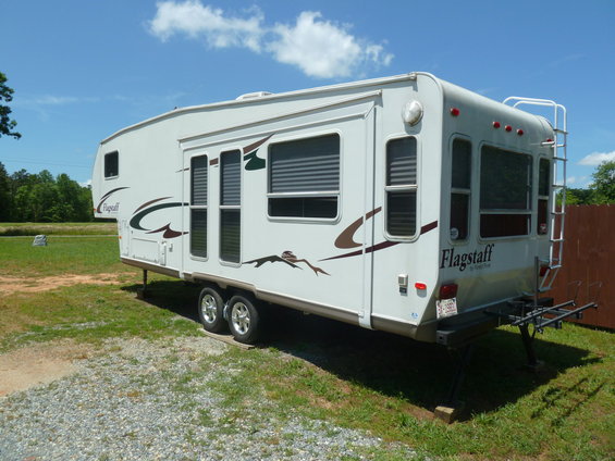 White Flagstaff camper trailer with brown graphics, parked on grass with a ladder on the rear