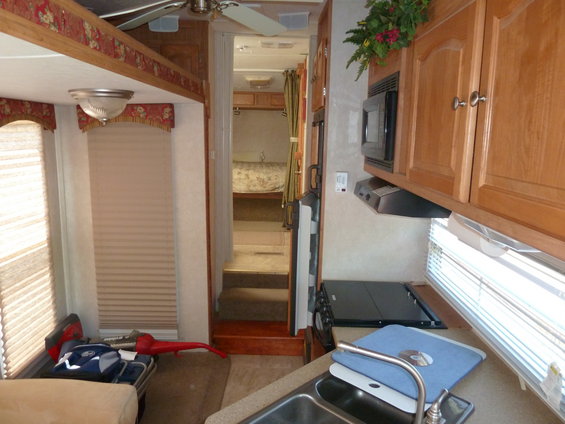 Camper interior showing a sink, counter, microwave, and a hallway leading to a bedroom