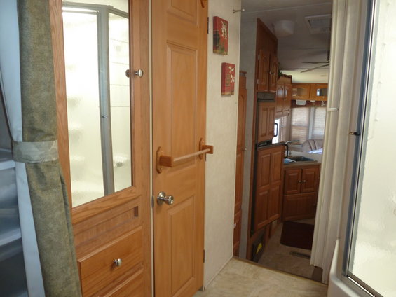 Interior view of a camper RV showing a shower stall, wooden cabinets, and a sink area