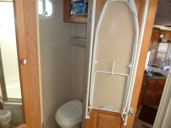 RV bathroom with toilet, shower stall, and a fold-down ironing board mounted on the door