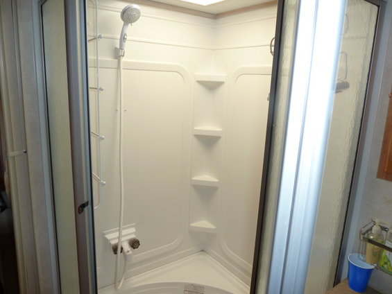 RV shower stall with white walls, shelves, and a shower head