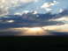1994 Ford Bronco - Sunbeams pierce dramatic clouds at sunset, illuminating distant mountains and a dark foreground field.