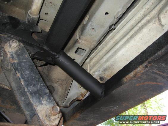 Underbody of a vehicle showing black metal tubing and rusty frame components