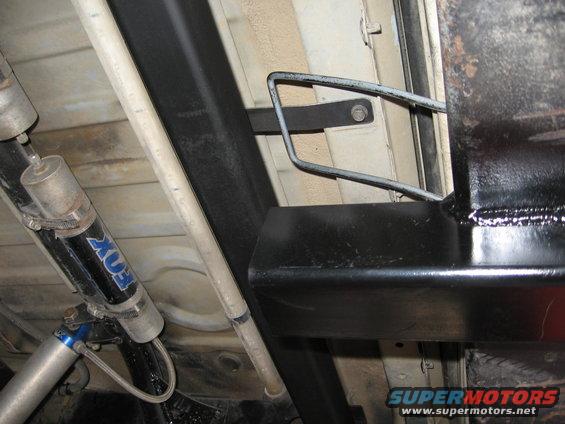 Underside view of a vehicle's rear bumper and suspension, showing black metal brackets and a FOX shock absorber