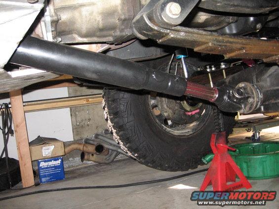 Underside view of a vehicle's driveshaft connecting to the differential, with a tire and exhaust visible