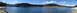 1994 Ford Bronco - A vast expanse of water is bordered by trees and hills under a bright, cloud-dotted sky.