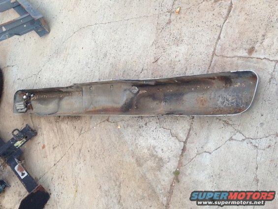 Rusted metal bumper section with chrome trim on the right end, lying on concrete