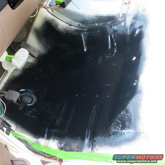 Interior floor pan sprayed with black coating, showing pedals and wiring