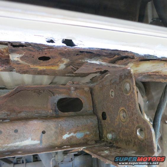 Heavily rusted frame section of a vehicle, showing significant corrosion and holes