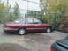 1992 Ford Crown Victoria - Maroon 1992 Ford Crown Victoria parked beside a fence with trees and a building in the background.