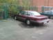 1992 Ford Crown Victoria - A maroon 1992 Ford Crown Victoria is parked in a lot next to a chain-link fence with barbed wire.