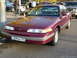 1992 Ford Crown Victoria - A maroon 1992 Ford Crown Victoria is parked on the street, with other vehicles and pedestrians in the background.