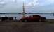 1992 Ford Crown Victoria - A red sedan sits by the water with boats and a tall bell tower in the distance.