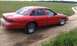 1992 Ford Crown Victoria - A red 1992 Ford Crown Victoria sedan is parked on a dirt road with grassy fields in the background.