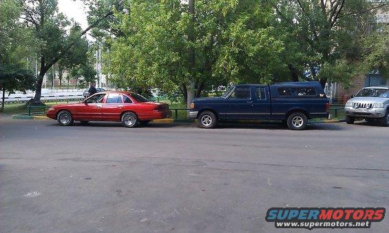 Red sedan parked next to a blue pickup truck with a camper shell. A silver SUV is parked to the right