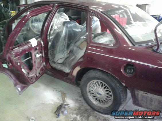 Maroon sedan with doors open and interior covered in plastic, parked inside