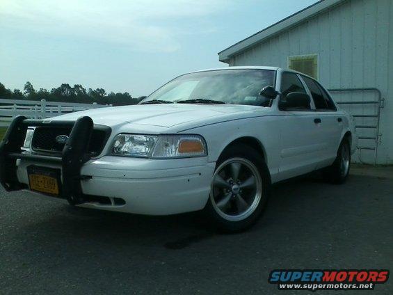 White Ford Crown Victoria with a push bar and aftermarket wheels parked outside a building