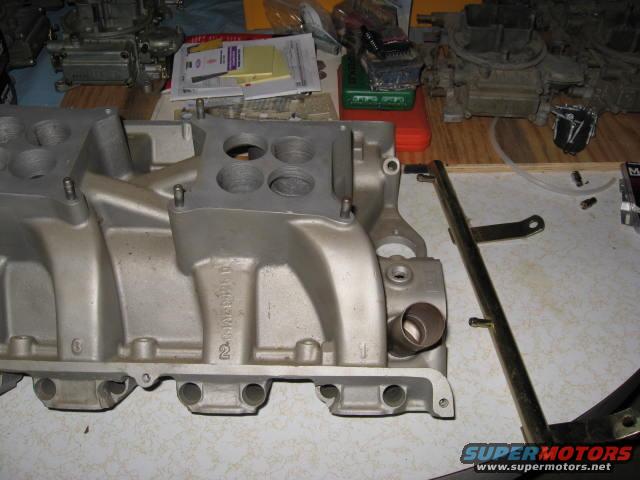 Aluminum intake manifold on a workbench with carburetors and parts in the background
