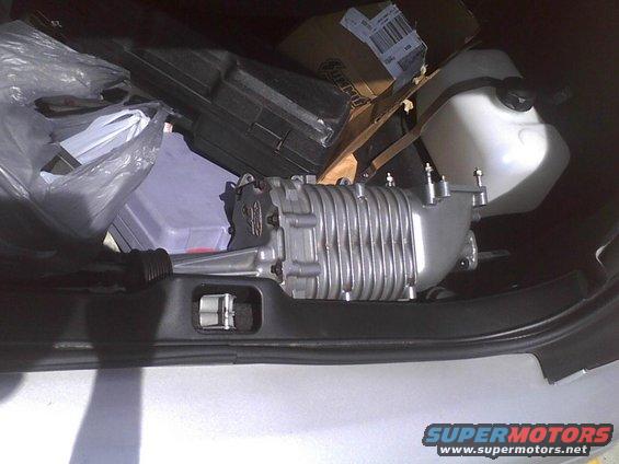 Silver supercharger and plastic storage bin in car trunk with boxes and a white tank
