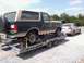 1991 Ford Bronco - A dark green and tan Ford Bronco is loaded onto a car trailer, with a sedan visible behind it.