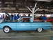 1963 Ford Ranchero - A light blue 1963 Ford Ranchero is displayed with its hood open, alongside other vehicles at an indoor event.
