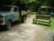 1979 Ford Bronco - A vintage Ford F-Series truck sits parked on a gravel driveway near a rustic wooden bench and outbuildings.