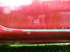 1993 Mazda MX-3 - The lower body panel of a red car shows wear and tear, with visible paint damage and white spots.