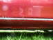 1993 Mazda MX-3 - Close-up of a red car's lower side panel showing signs of wear and tear, possibly, rust.